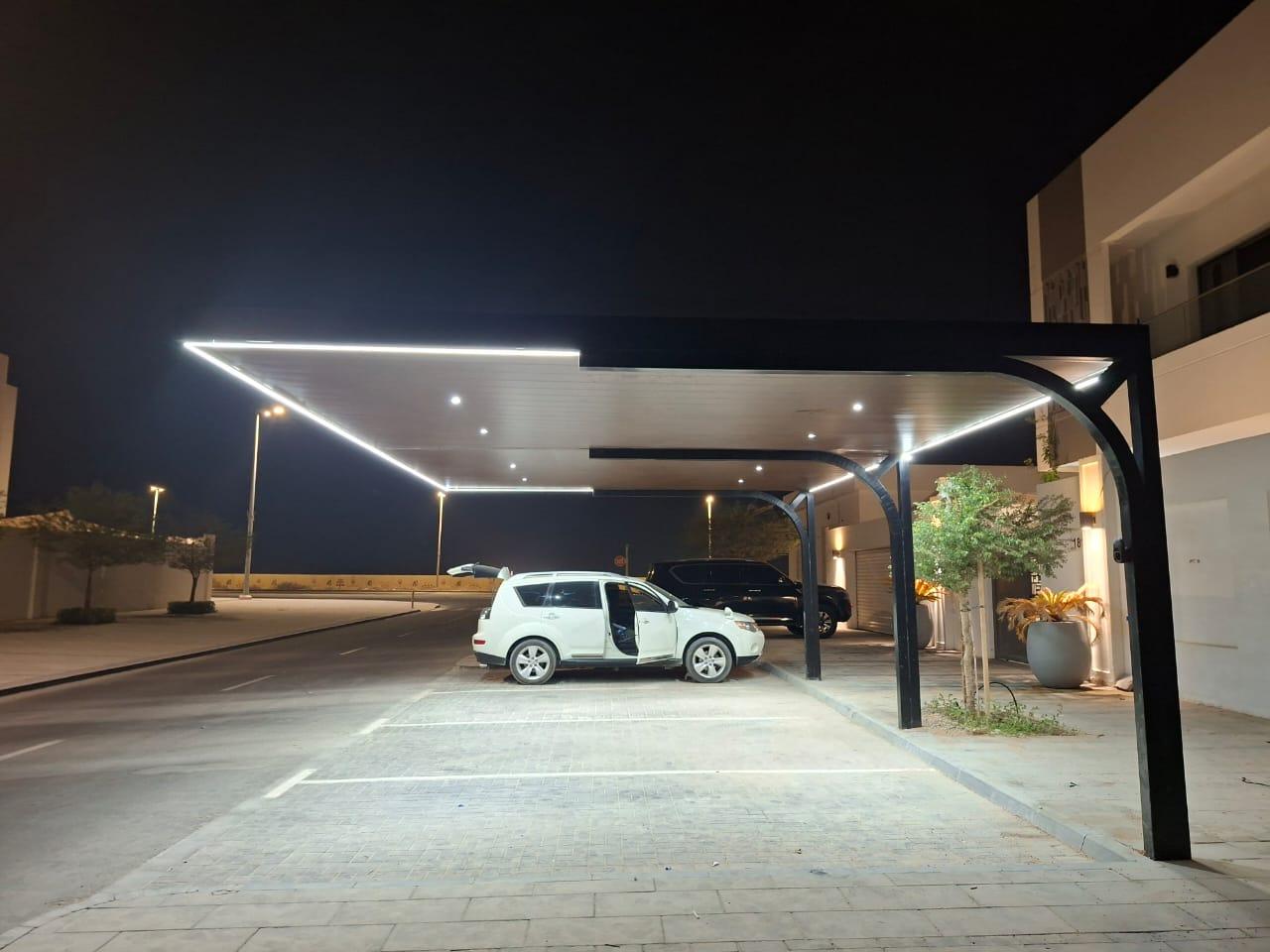 Cantilever parking shed with LED edge lighting over parked SUVs at night