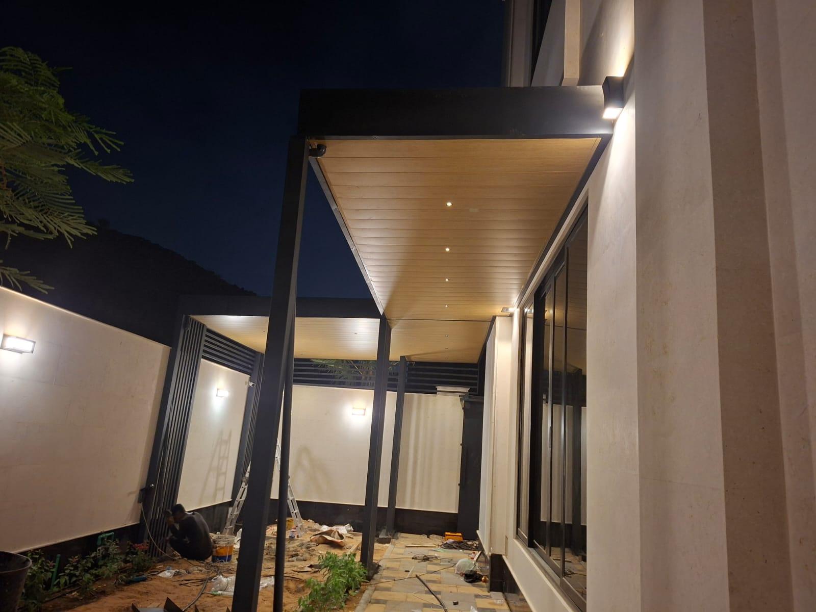 Night view of a custom steel pergola with wood-look ceiling and integrated LED lighting