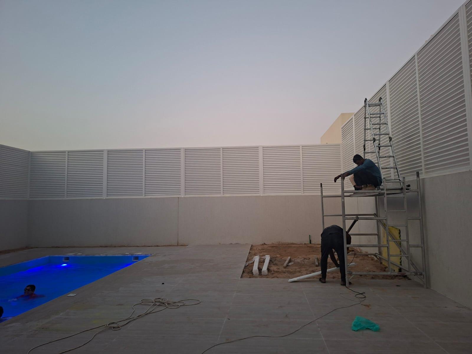 Crew installing a white louvered privacy fence beside a villa pool